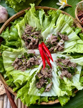 Thai ground beef lettuce wraps on a bamboo mat garnished with red chili and herbs.