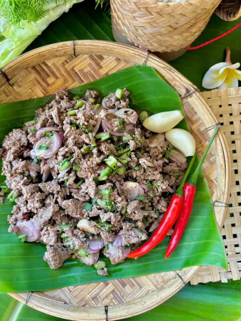 Thai ground beef salad on a banana leaf, surrounded by lettuce, dill, and sticky rice.