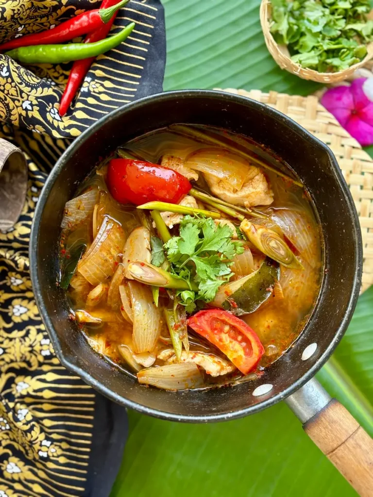 Thai lemongrass soup with tomato, coriander, onion, galangal, and kaffir lime leaves served in a pot.