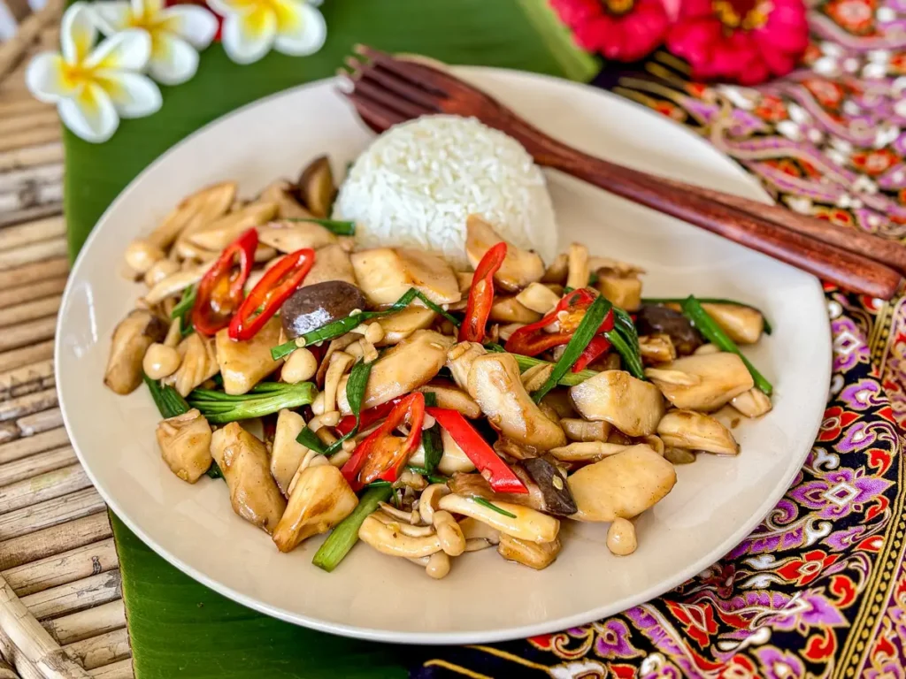 Pad hed, Thai mushroom stir fry with chili, green onions, and rice on a white plate, served with wooden cutlery.