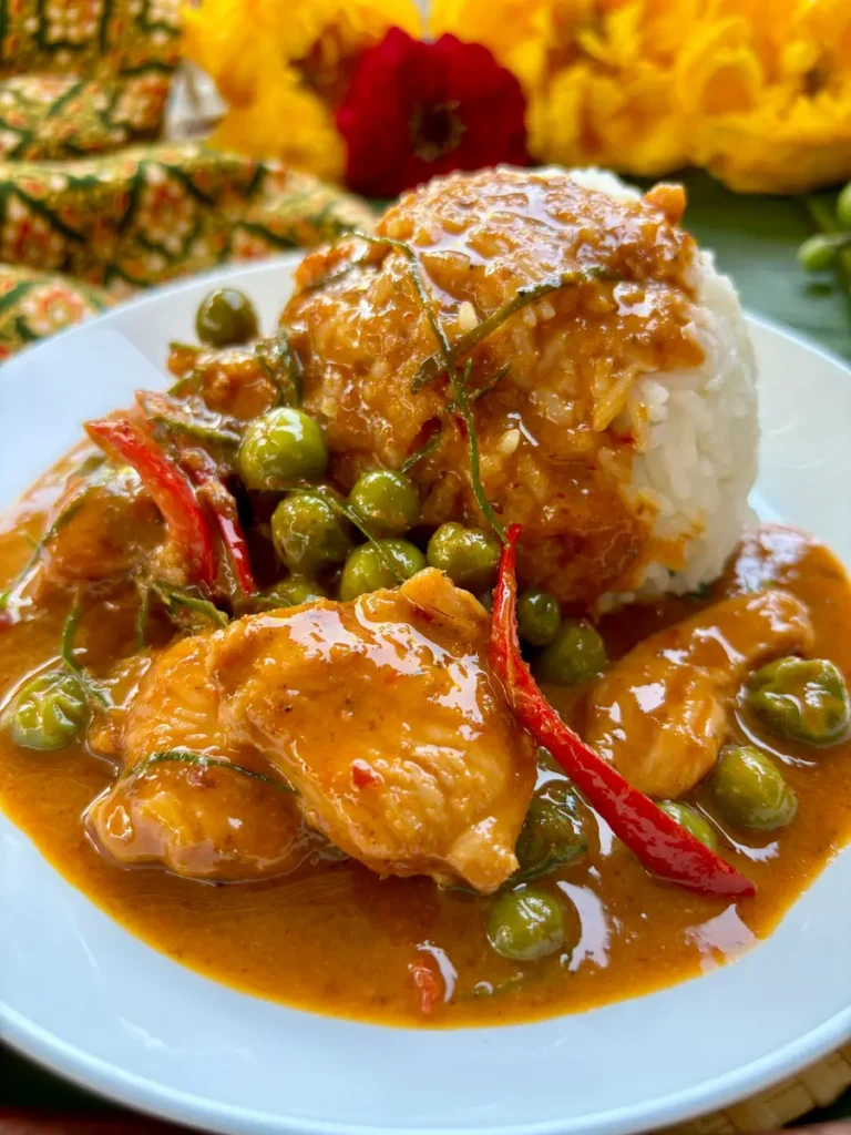 Gaeng panang chicken with pea beans and red chili with jasmine rice served on a white plate.