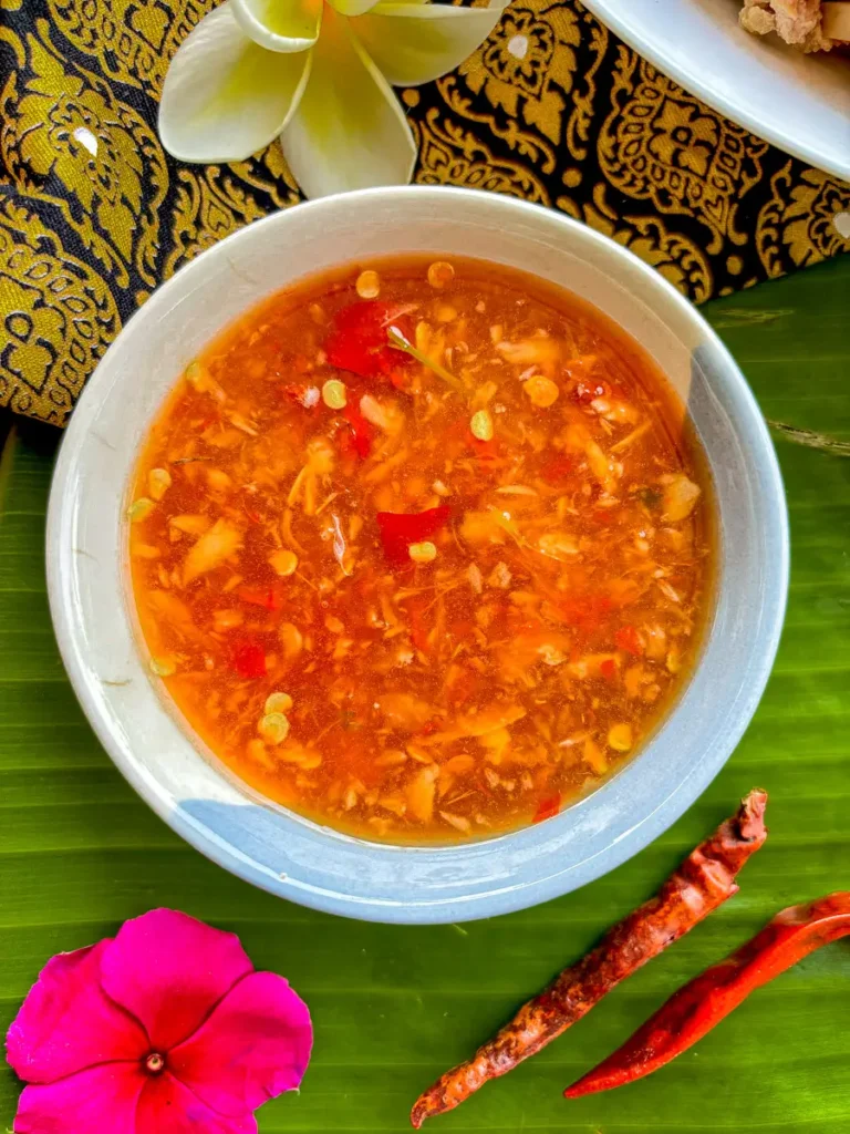 Bowl of sour Thai salad dressing on banana leaf with floral decor.