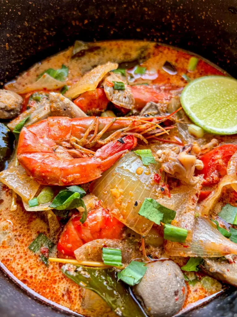 Thai tom yum talay soup surrounded by dried chilies, shallots, and tropical flowers.