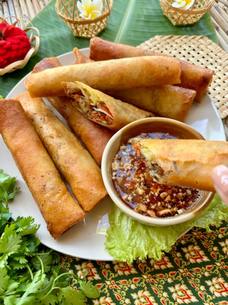 Thai spring rolls with dipping sauce on the side, and a hand dipping a half-eaten roll into the sauce.