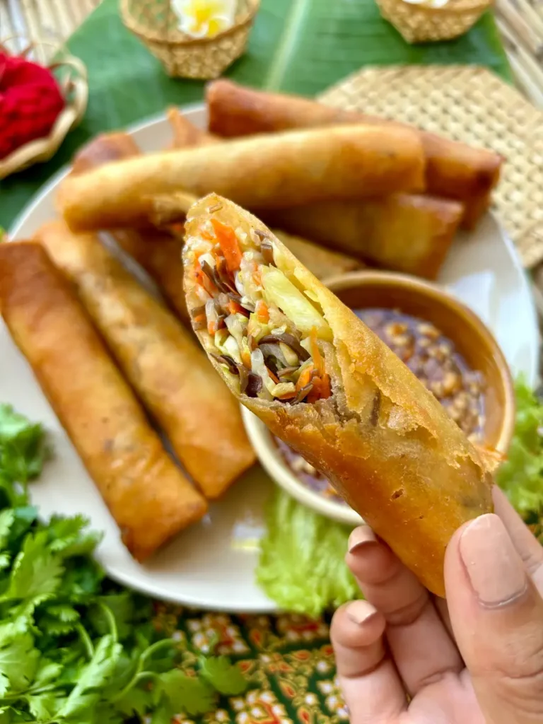 Close-up of a hand holding a half-eaten Thai spring roll with vegetables filling.