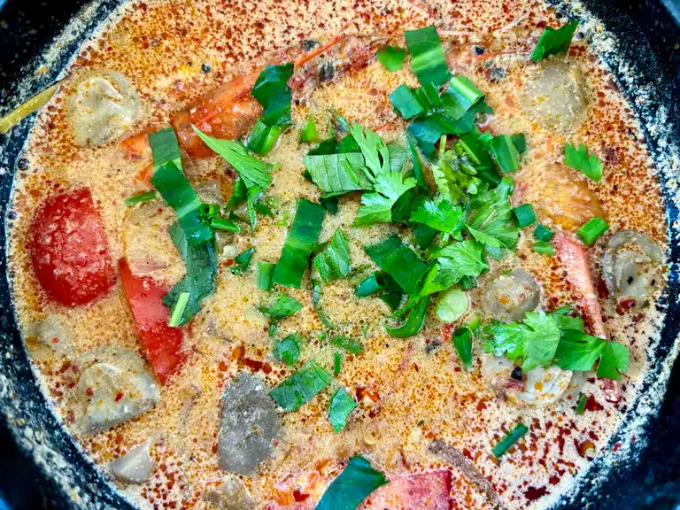 Tom yum talay soup in a cooking pot, garnished with fresh herbs, ready to serve.