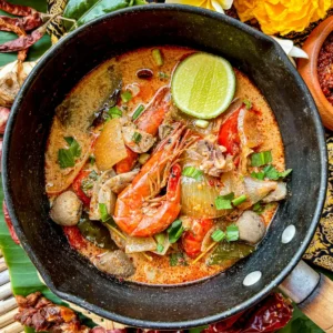 Tom yum talay Thai seafood soup in a black pot with prawns, lime, mushrooms, and fresh herbs.