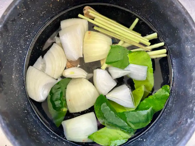 Pot with onions, kaffir lime leaves, lemongrass, and galangal ready for cooking.