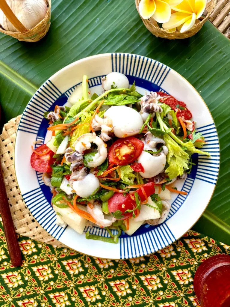 Traditional Thai squid salad, yum pla muk, on a white dish set against a patterned fabric and banana leaf.