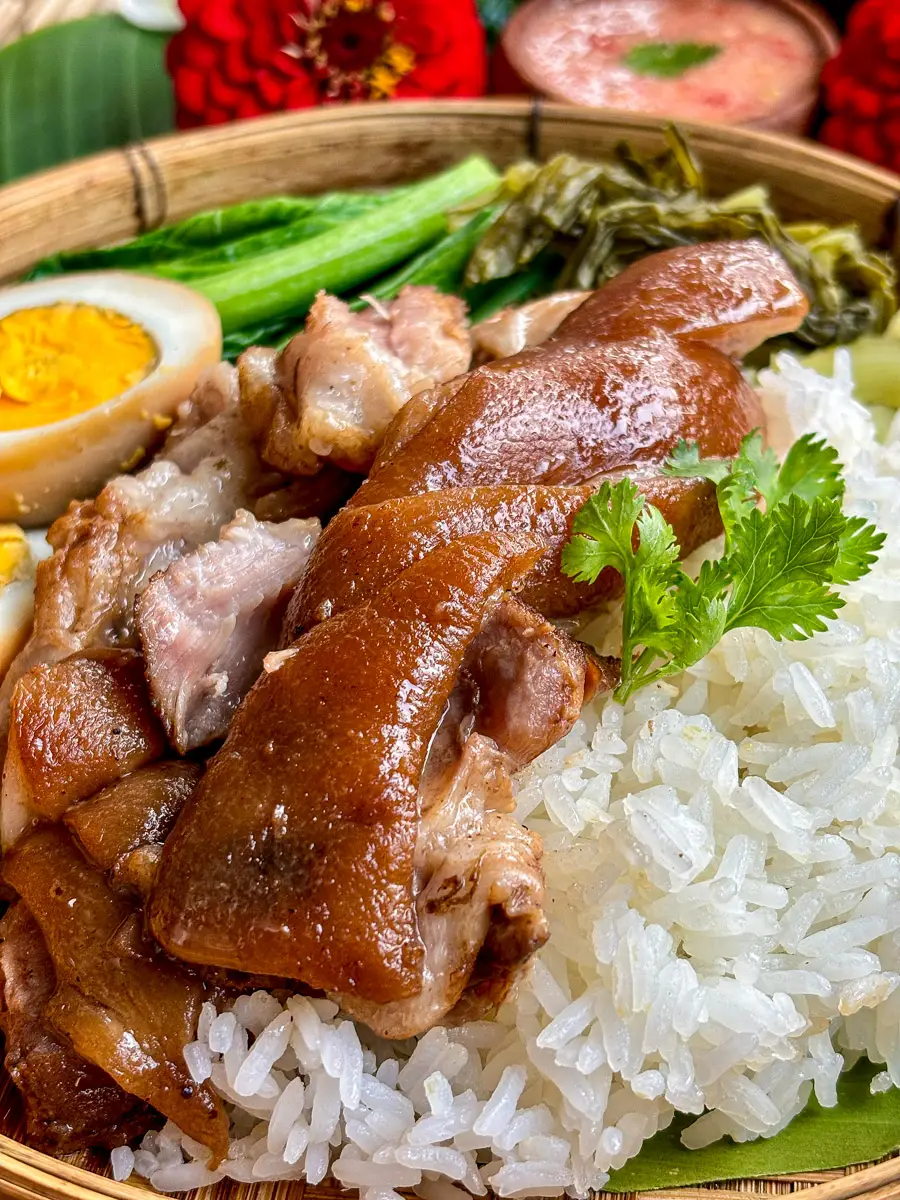 Braised pork leg slices on rice, served with boiled egg, pickled greens, and cilantro garnish.