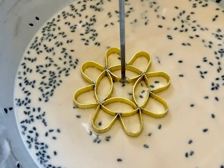 Lotus cookie mold above batter sprinkled with black sesame seeds.