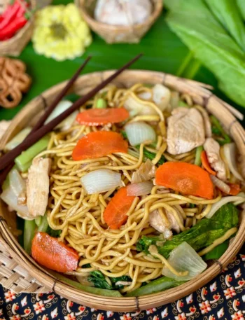 Chicken egg noodle stir-fry, pad mee luang, with vegetables in a bamboo dish.