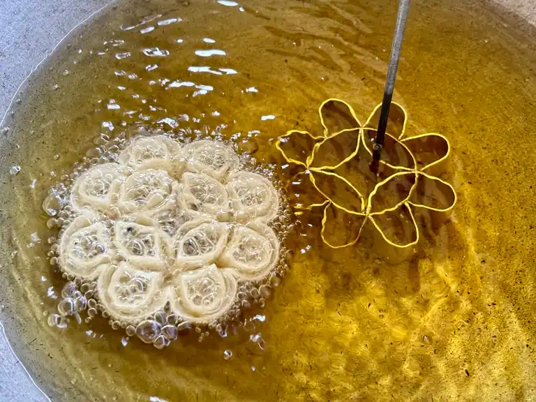 Lotus cookie frying in oil with brass mold next to it.