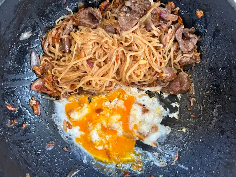 Egg and beef noodles stir-fried in a wok.