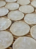 Dusted gyoza wrappers on a bamboo surface.
