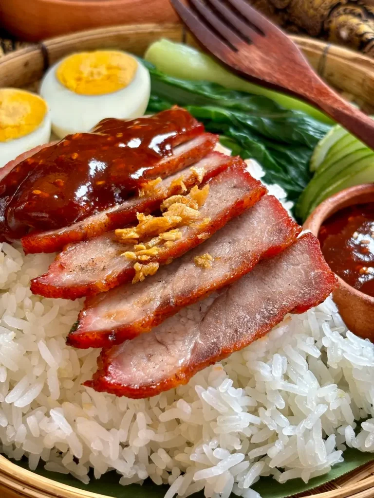 Close-up of khao moo dang with Thai red pork, red sauce, steamed rice, and boiled eggs.