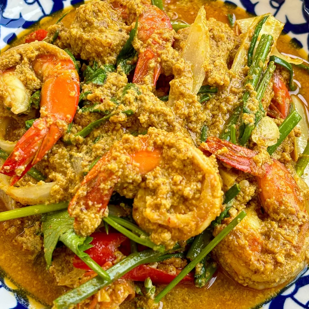 Koong karee, Thai shrimp yellow curry with egg and vegetables in a patterned blue bowl.