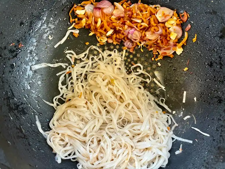 Wide rice noodles with garlic and shallots in a wok.