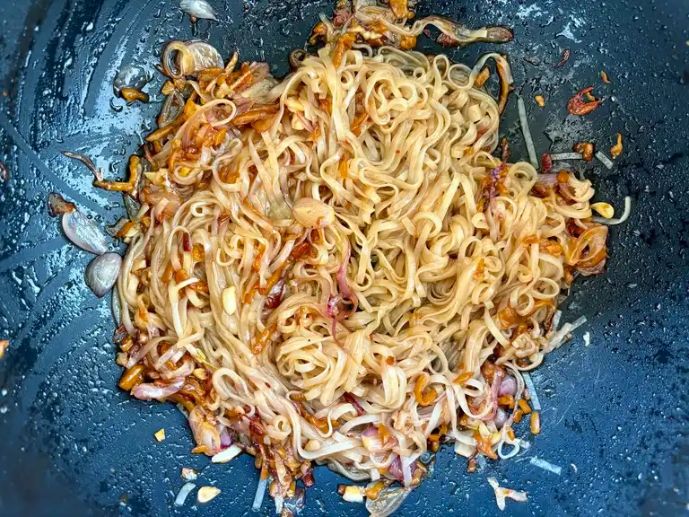 Noodles tossed with garlic and shallots in wok.