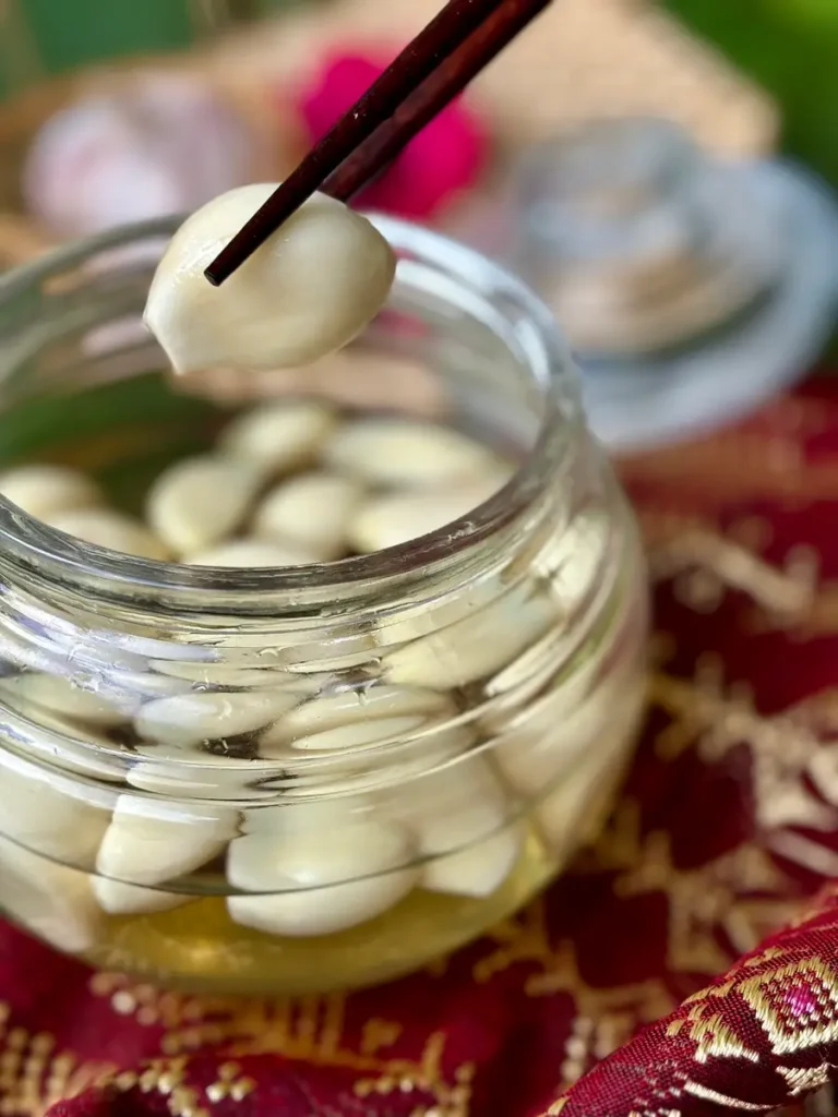 Pickled garlic in a glass jar with clear brine and chopsticks lifting a single clove.
