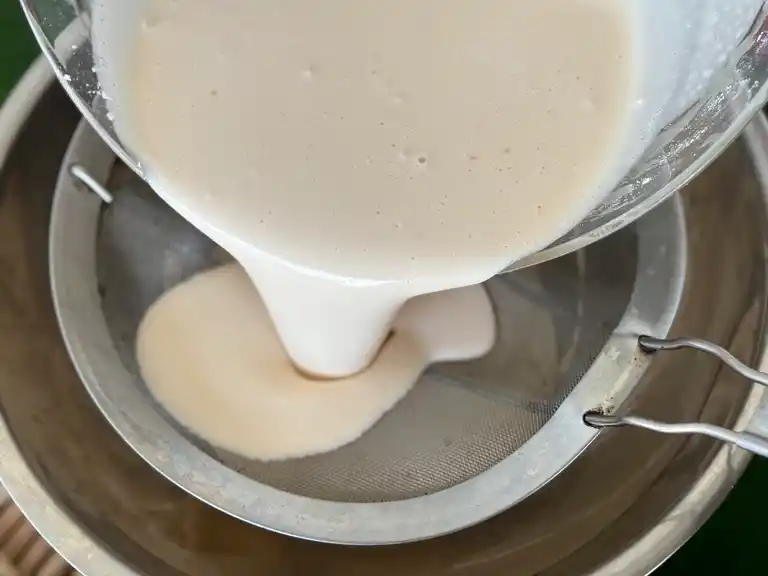 Pouring Thai lotus cookie batter through a sieve.
