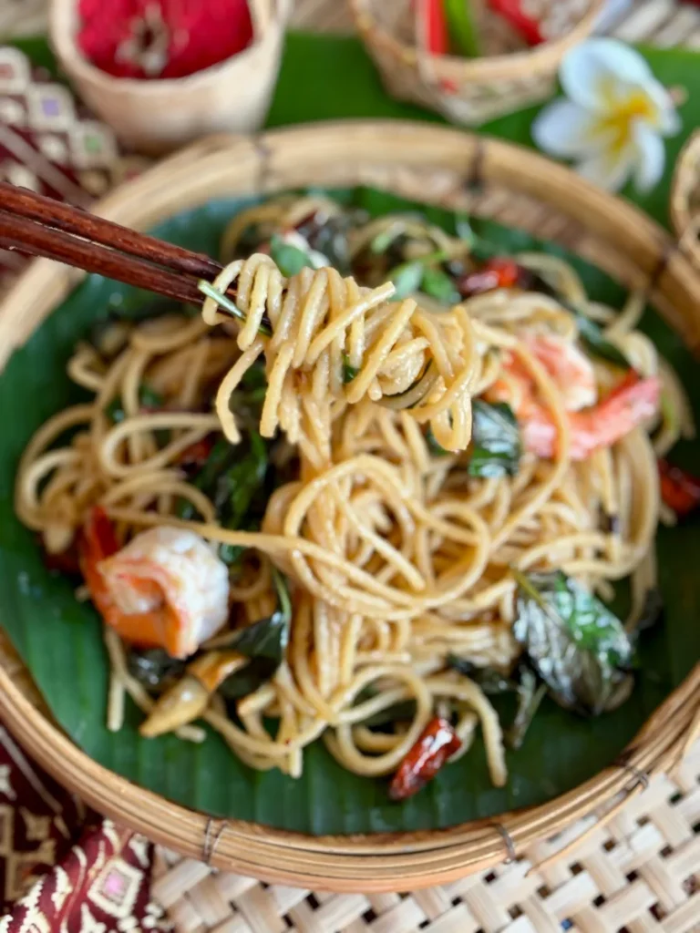 Spaghetti noodles lifted over a bamboo dish with shrimp and more pasta.