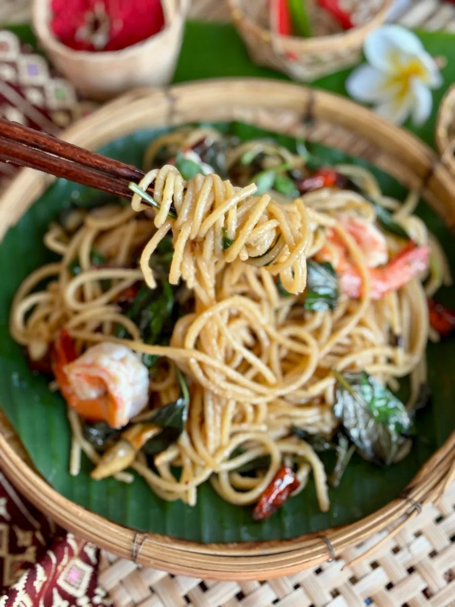 Spaghetti noodles lifted over a bamboo dish with shrimp and more pasta.