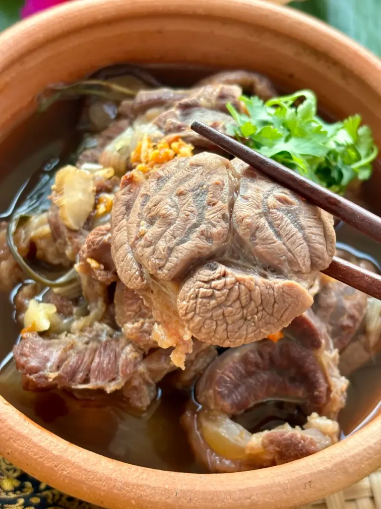 Close-up of Thai beef stew with chopsticks lifting cooked beef shank.