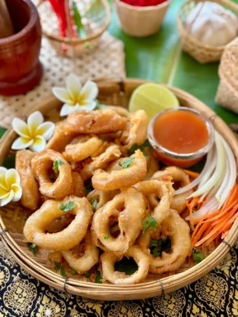 Thai calamari served in a traditional bamboo basket, garnished with fresh coriander and accompanied by sweet chili sauce and lime wedges.