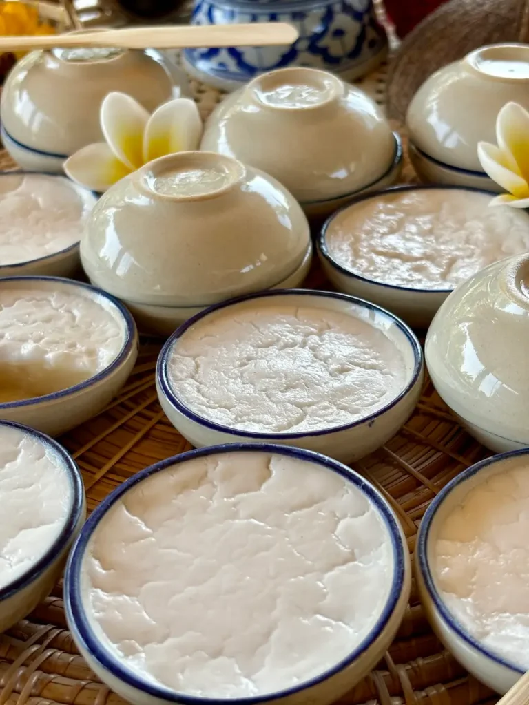 Thai coconut custard dessert in ceramic cups with plumeria flowers.