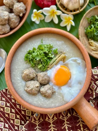Thai congee, jok rice porridge, with pork meatballs, garnished with green onions and coriander with egg.