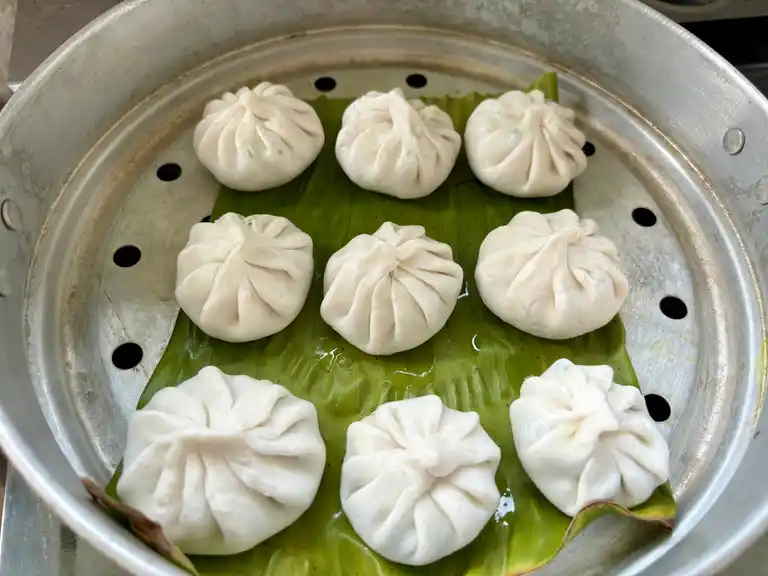 Uncooked garlic chive dumplings arranged on a banana leaf in a steamer.
