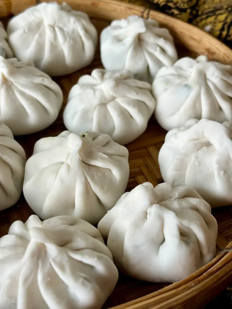 Uncooked Thai garlic chive dumplings on a woven bamboo mat.