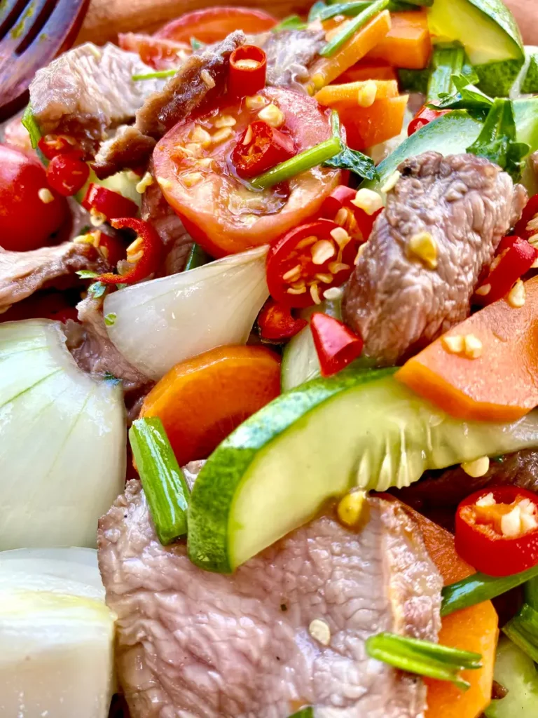 Close-up of yum neua with grilled steak slices, carrots, chilies, and onions, all coated in a dressing.