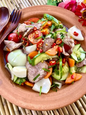 Yum neua, Thai beef salad, with vegetables like carrots, cucumbers, and onion.