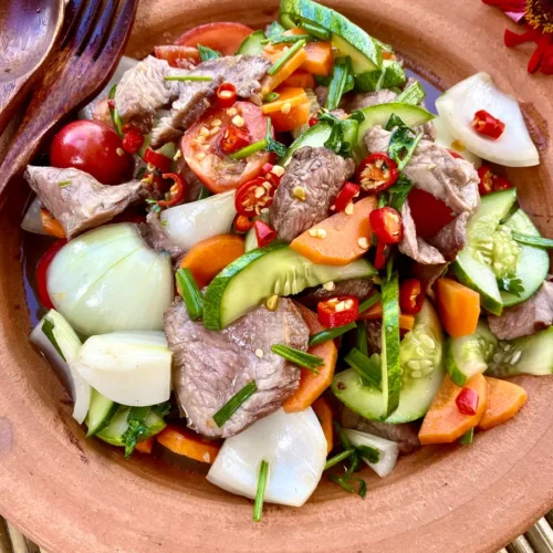 Yum neua, Thai beef salad, with vegetables like carrots, cucumbers, and onion.