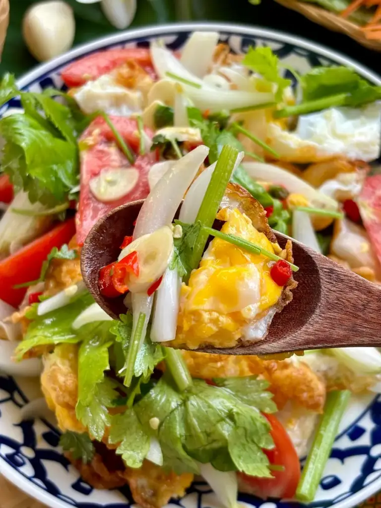 Close-up of Thai fried egg salad, or yum kai dao, with a spoon lifting egg and vegetables.