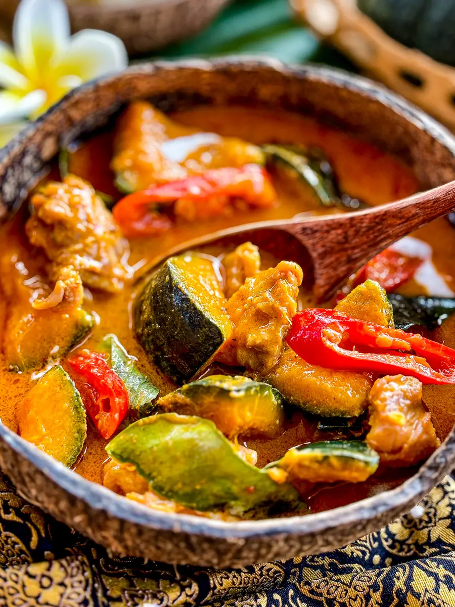 Thai kabocha squash curry with chicken and red chilies in a creamy coconut sauce, served in a rustic coconut bowl.