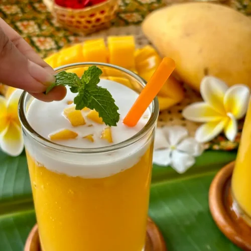 Thai mango shake in a tall glass with a layer of coconut milk.