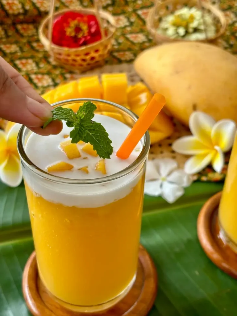 Thai mango shake in a tall glass with a layer of coconut milk.