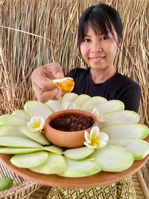 Thai woman presenting a plate of sliced green mango with sweet chili dip.