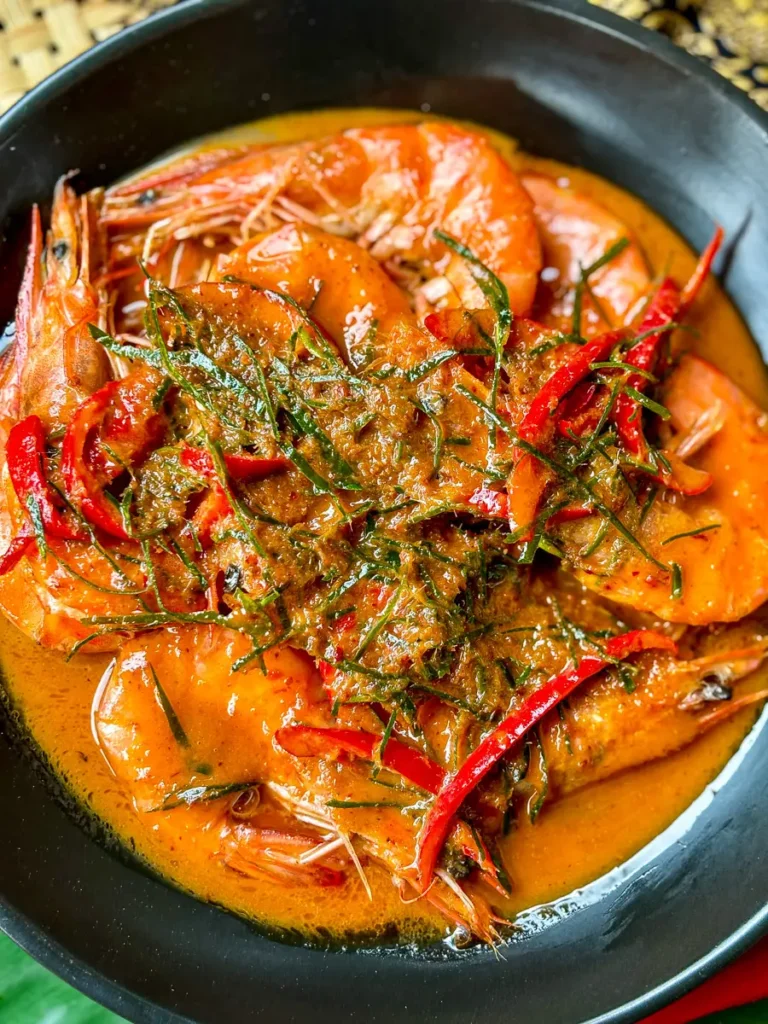 Choo chee shrimp in creamy red curry sauce, served in a black bowl with kaffir lime and sliced chili on top.