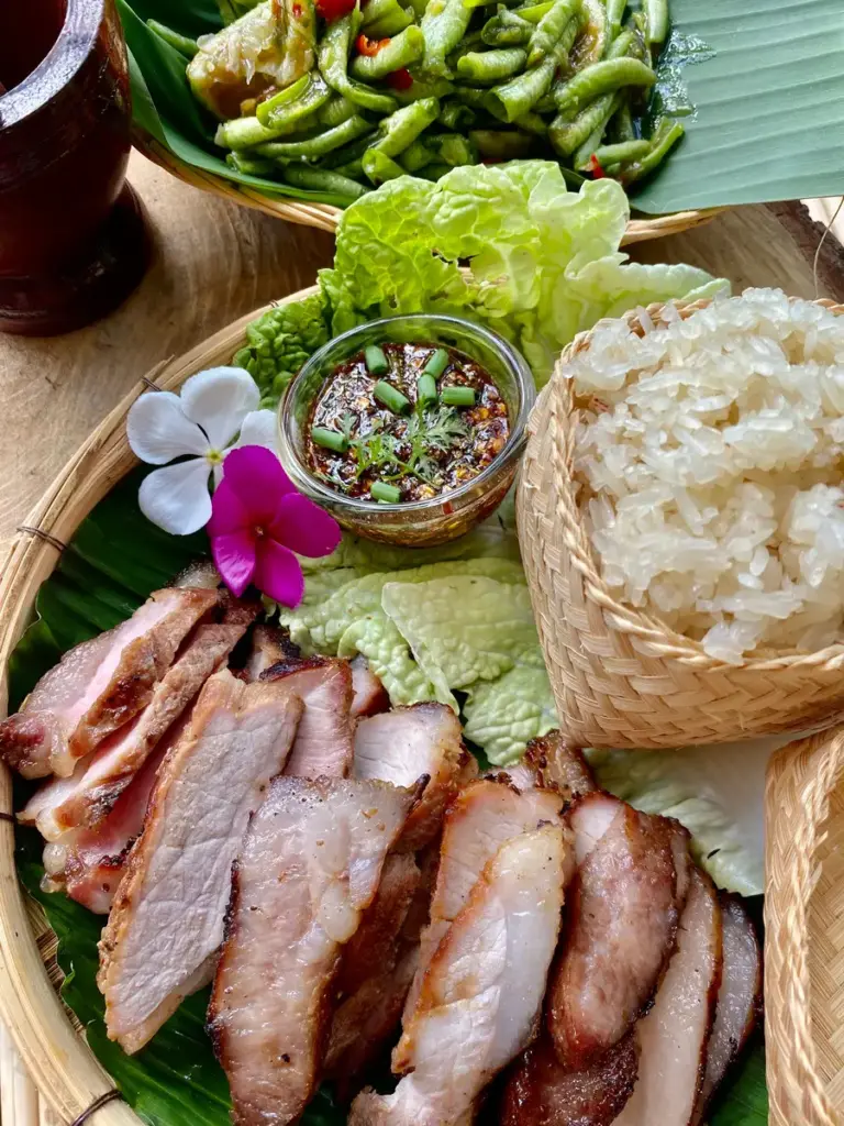 Moo yang, Thai grilled pork, served with dipping sauce, Thai sticky rice, and papaya salad.