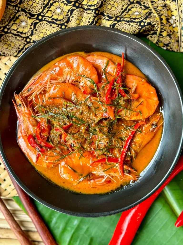 Traditional Thai choo chee curry featuring whole shrimp in thick red coconut curry, garnished with herbs and chili.