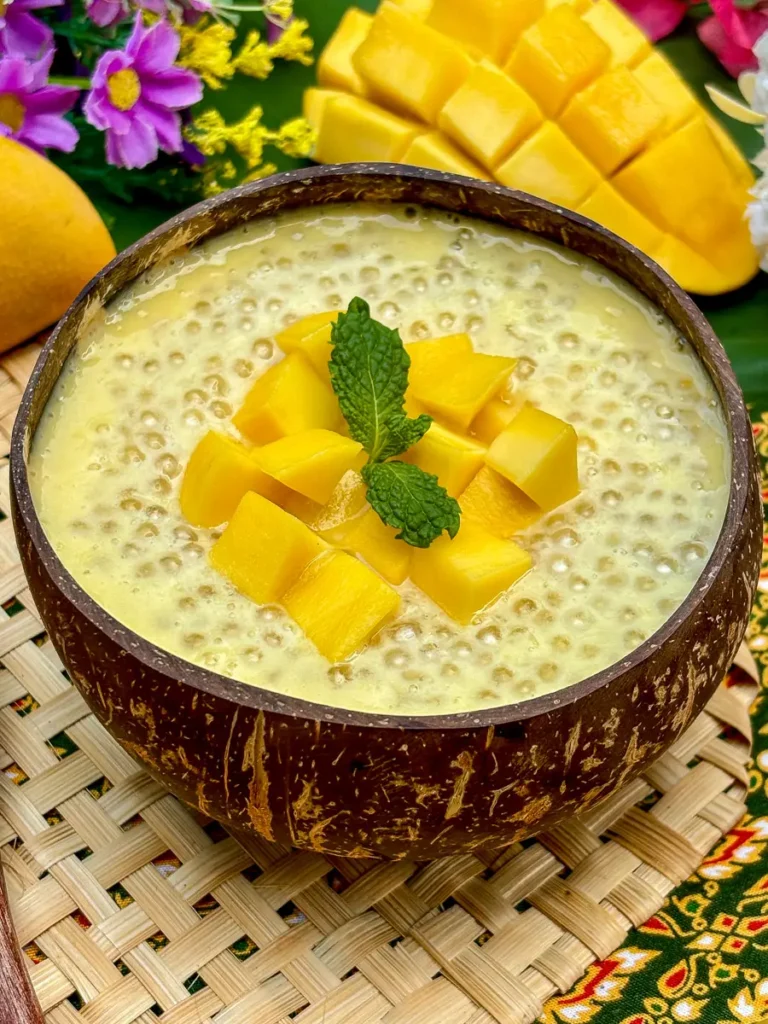Mango sago dessert served in a coconut shell, topped with mango cubes and a mint leaf.