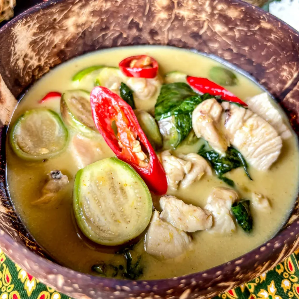 Close-up of Thai eggplant green curry with chicken, Thai eggplants, and red chili in a coconut milk-based sauce.