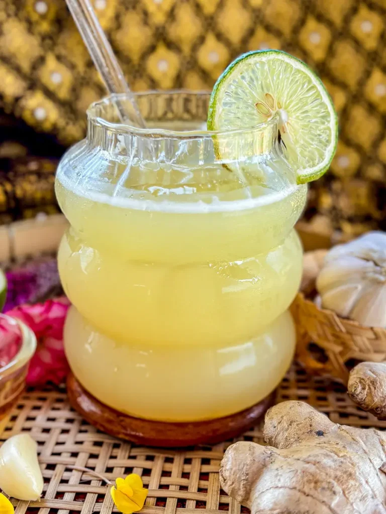 Close-up of a glass of iced ginger garlic tea with a lime slice, served with fresh ginger, garlic, and honey on the side.
