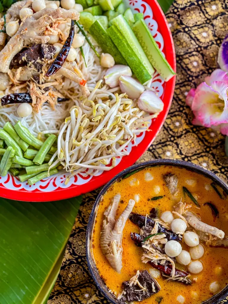Top view of Thai chicken feet curry paired with fresh vegetables and vermicelli noodles on a colorful serving plate.