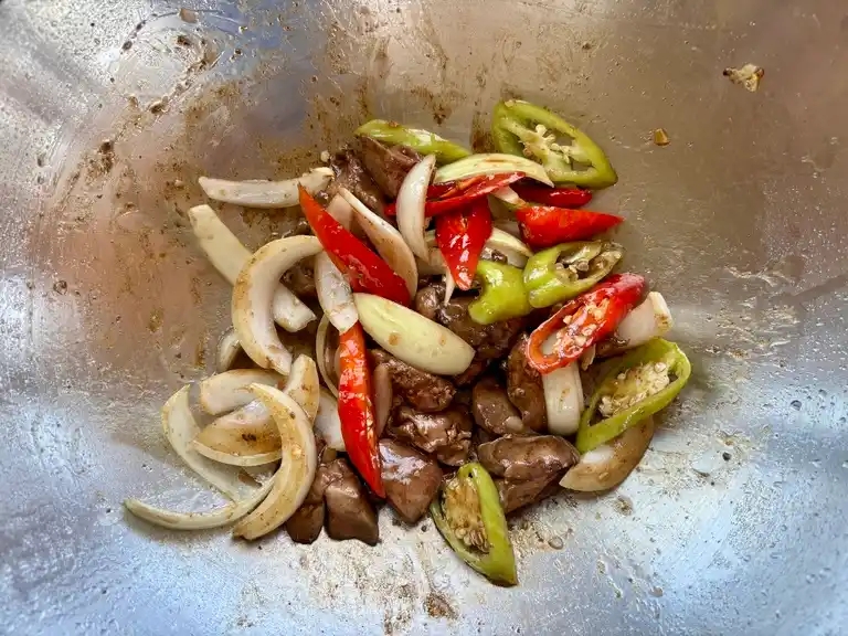 Stir-fried chicken liver with chillies, onion and garlic in a wok.