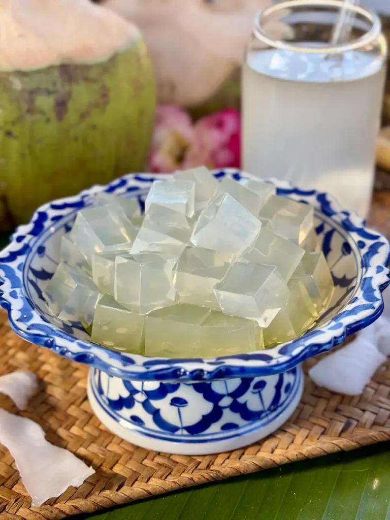 Coconut jelly cubes in a blue and white bowl, served alongside fresh coconut water in a glass, with a green coconut in the background.